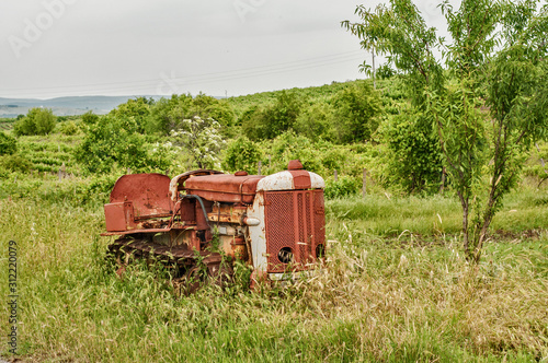 Old neglected rusty small vintage caterpillar tractor on green meadow