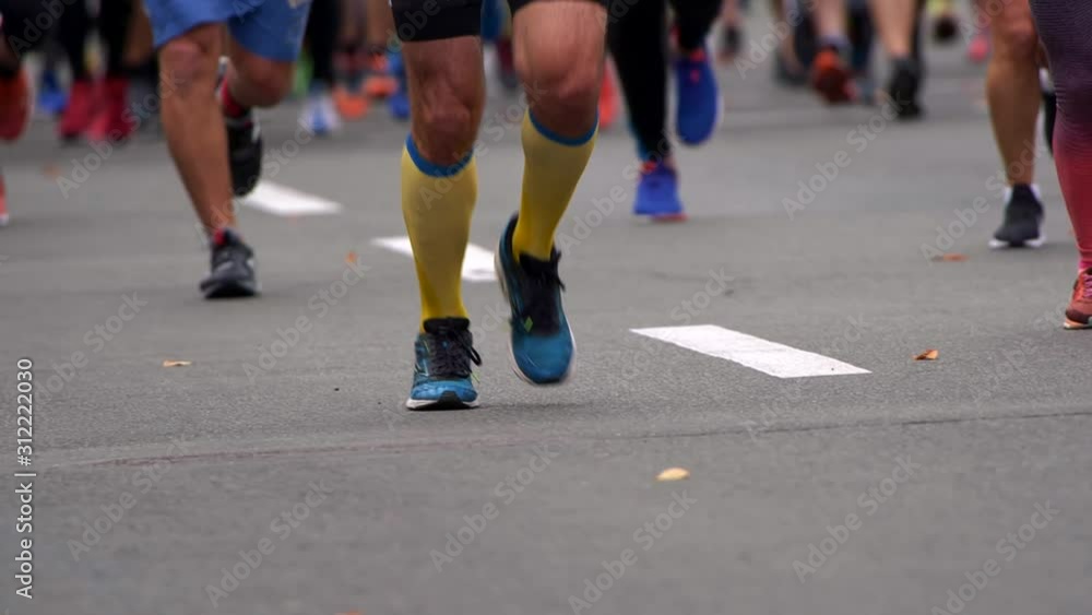 Crowd of people running in city marathon. Men and women wearing sportswear. Lower part of bodies. Legs with straining and relaxing muscles. Slow motion shot Crowd of people running in city marathon. Men and women wearing sportswear. Lower part of bodies. Legs with straining and relaxing muscles. Slow motion shot