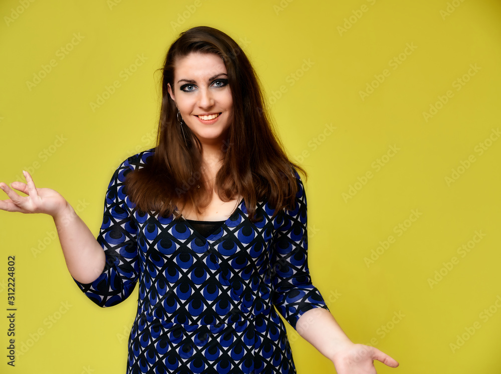 Portrait of a pretty brunette woman with a beautiful hairstyle and with excellent makeup in a dark blue blouse on a yellow background. It stands showing hands with a smile in front of the camera. Portrait of a pretty brunette woman with a beautiful hairstyle and with excellent makeup in a dark blue blouse on a yellow background. It stands showing hands with a smile in front of the camera.
