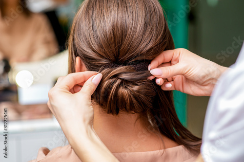 Hairdresser's hands making hairstyle for woman in beauty salon, rear view, back view.