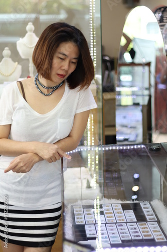 Asian short hair woman which is customer choosing and looking for jewellery gift for her special day with happy face. woman wearing beautiful natural pearl necklace in jewellery store