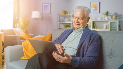 Photography Progressive Senior Man at Home Sitting on Sofa Uses Laptop Computer