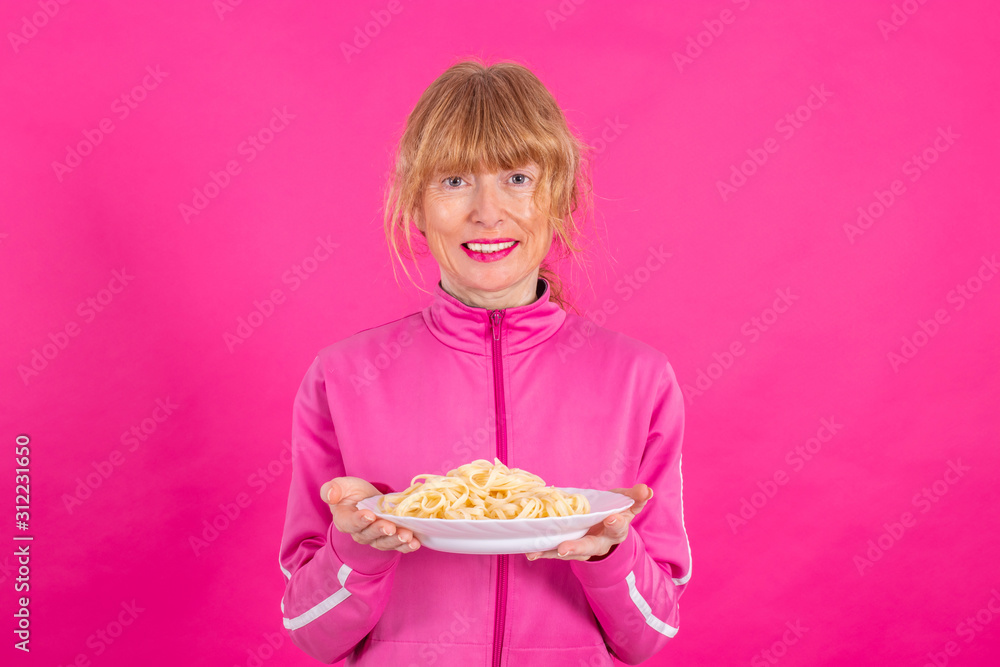 smiling adult woman with sportswear and plate of skin isolated pasta on pink background smiling adult woman with sportswear and plate of skin isolated pasta on pink background