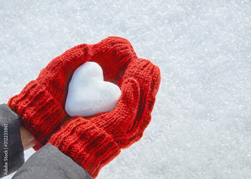 Female hands in knitted mittens with heart of snow in winter day. Love concept. Valentine day background.