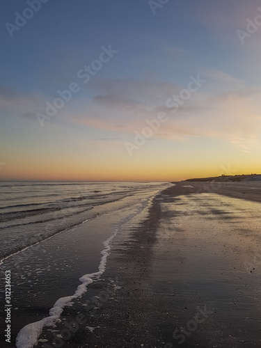 Coastline at sand beach with orange colors from the sun in the horizon. View lengthwise of the shore. Sæby, Denmark.