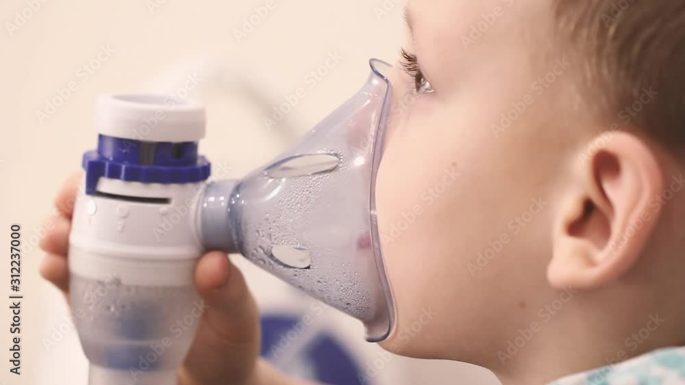 Child with asthma problems making inhalation with mask on face and coughing. Sick kid a respiratory infection or bronchitis and breathes heavily. Treatment of pneumonia nebulizer at home. Close up Child with asthma problems making inhalation with mask on face and coughing. Sick kid a respiratory infection or bronchitis and breathes heavily. Treatment of pneumonia nebulizer at home. Close up