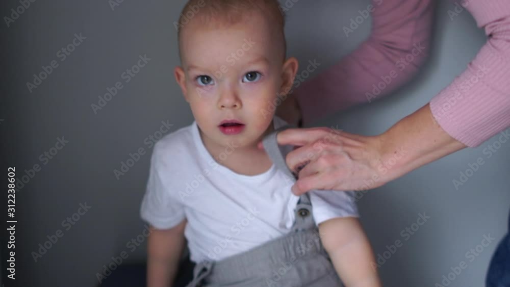 Close portrait of a mom helps a two year old boy to dress. Toddler education, happy family Close portrait of a mom helps a two year old boy to dress. Toddler education, happy family