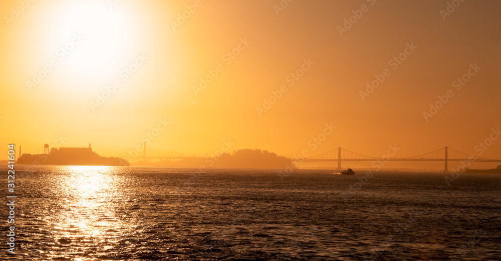 Early morning in the San Francisco Bay with Alcatraz Island , Bay Bridge and Treasure Island in silhouette with a fishing boat heading out to sea