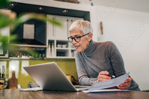 Foto Charming woman holding papers and looking at laptop, portrait.