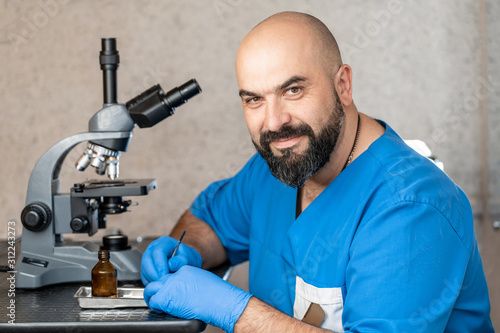 Male laboratory assistant examining biomaterial samples in a microscope.