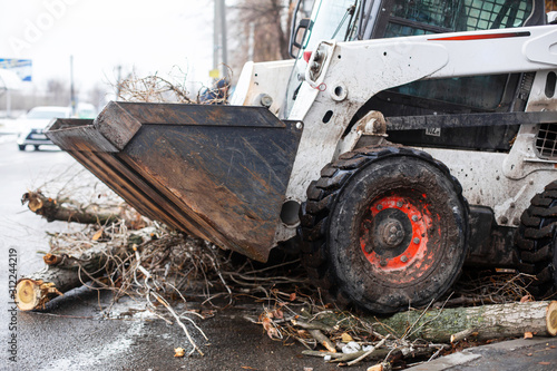 Urban emergency service removes a fallen tree on a road with special equipment traktor.