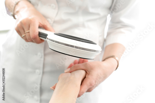 Dermatologist examines the condition of the skin of the patient hands with a dermatoscope, in a light cosmetology room photo