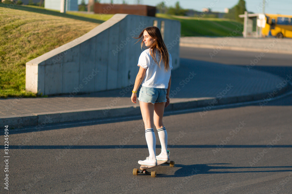 stylish girl in white stockings enjoy ride on longboard put hands up