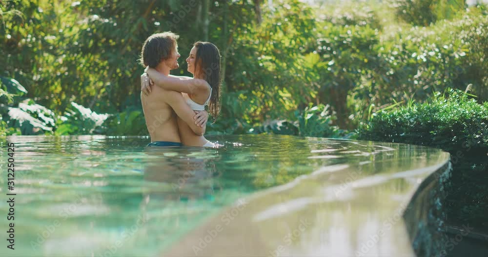 Happy diverse couple embracing and kissing in a beautiful jungle swimming pool on their tropical vacation together Happy diverse couple embracing and kissing in a beautiful jungle swimming pool on their tropical vacation together