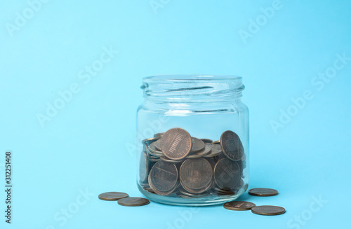 Glass jar with coins on light blue background