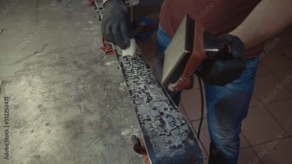 Applying hot wax to ski base with iron. Applying Ski Wax To Ski Base. Ski base tuning. Ski wax iron and wax bars. Ski service and repair. repairman in workshop ski service. Man Waxing Ski In Workshop Applying hot wax to ski base with iron. Applying Ski Wax To Ski Base. Ski base tuning. Ski wax iron and wax bars. Ski service and repair. repairman in workshop ski service. Man Waxing Ski In Workshop