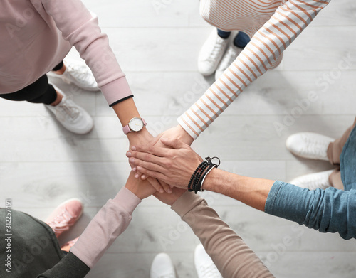 People holding hands together over light wooden background, top view. Unity concept