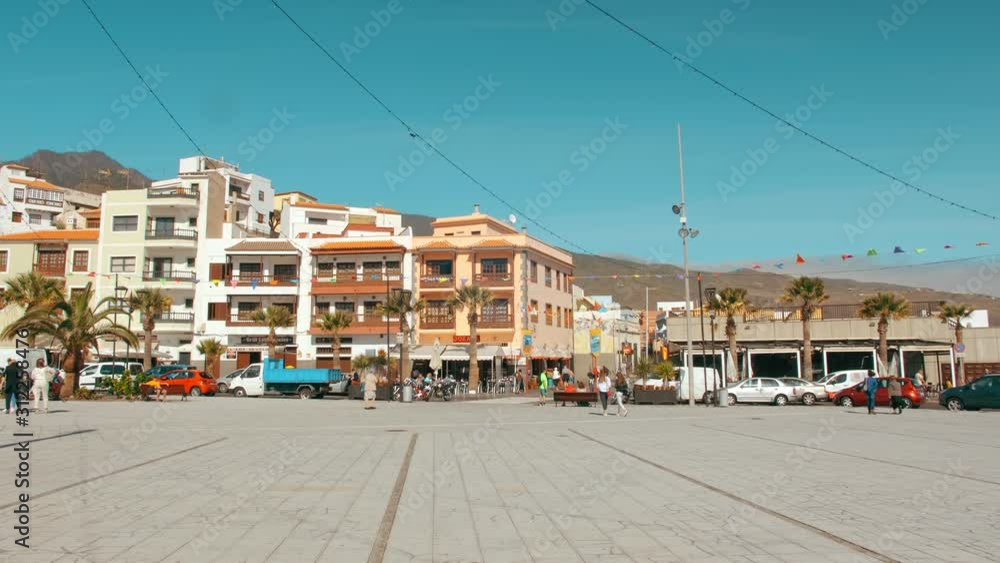Tenerife, Canary Islands, Spain - January, 2019: Spanish Latino square in the middle of a small town. Decorated with multicolored flags. A few typical houses and unrecognized locals. Tenerife, Canary Islands, Spain - January, 2019: Spanish Latino square in the middle of a small town. Decorated with multicolored flags. A few typical houses and unrecognized locals.