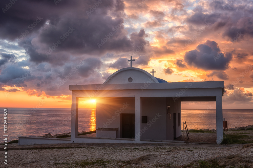 Cyprus Mediterranean seacoast at sunrise, amazing landscape with church, sky with colorful clouds and sun. Agioi Anargiroi (Kosmas and Damianos) chapel in Paralimni area, Cavo Greco, Ayia Napa