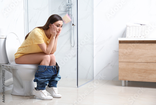 Upset woman sitting on toilet bowl in bathroom