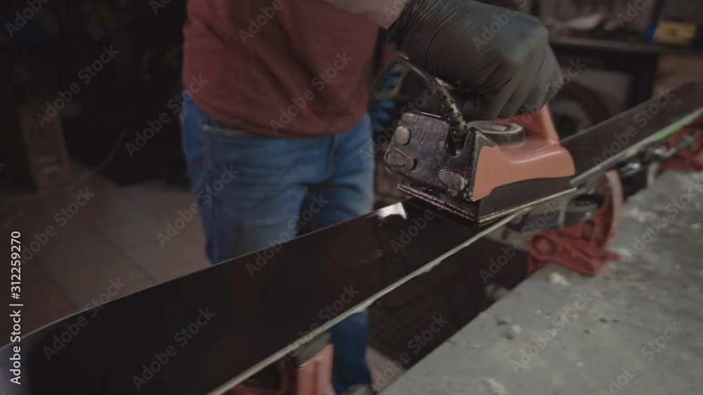 Applying hot wax to ski base with iron. Applying Ski Wax To Ski Base. Ski base tuning. Ski wax iron and wax bars. Ski service and repair. repairman in workshop ski service. Man Waxing Ski In Workshop Applying hot wax to ski base with iron. Applying Ski Wax To Ski Base. Ski base tuning. Ski wax iron and wax bars. Ski service and repair. repairman in workshop ski service. Man Waxing Ski In Workshop