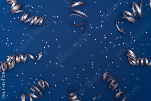 Festive composition with silver confetti and serpentine on trendy classic blue background. Celebration concept ideas for Christmas, New Year or any other holiday. Flat lay, copy space. Selective focus