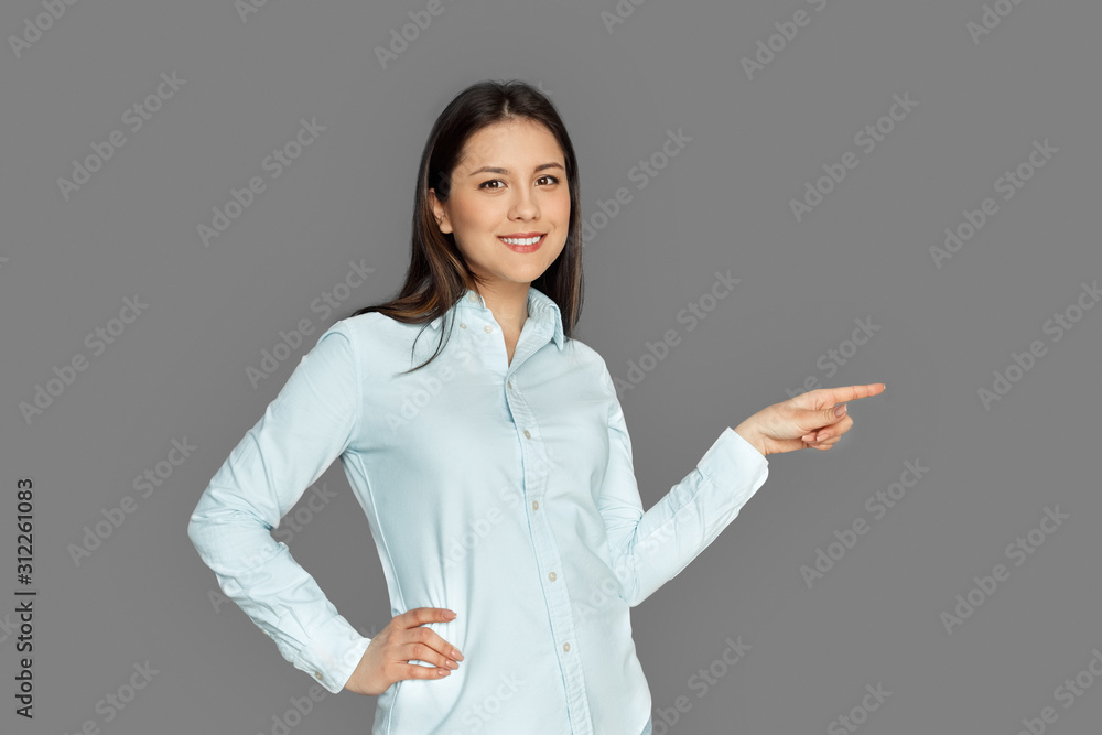 Space for Text or Product. Young woman standing isolated on grey pointing aside smiling happy Space for Text or Product. Young woman standing isolated on grey pointing aside smiling happy