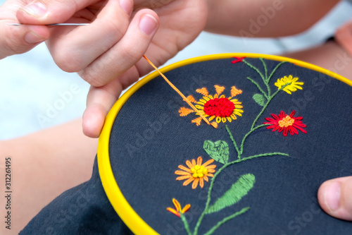 Women's hand embroidery in a hoop, a woman embroider a pattern on dark material. Close-up. The concept of needlework, hobby, leisure.