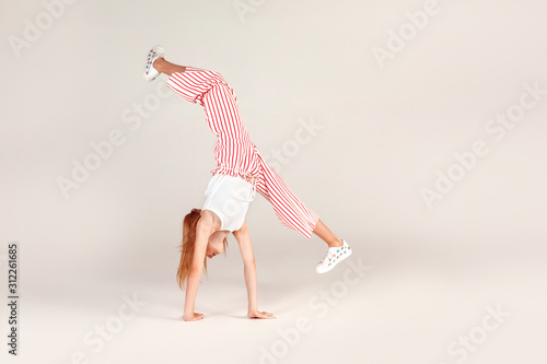 Inclusive Beauty. Girl with red hair isolated on grey doing front walkover concentrated