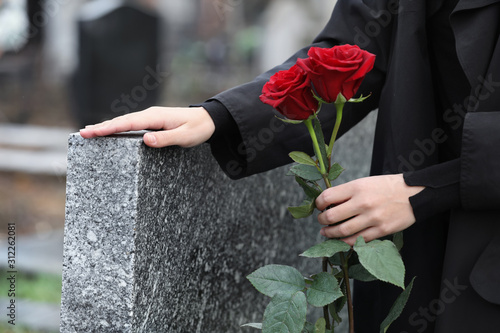 Fotografie Woman with red roses near grey granite tombstone outdoors, closeup