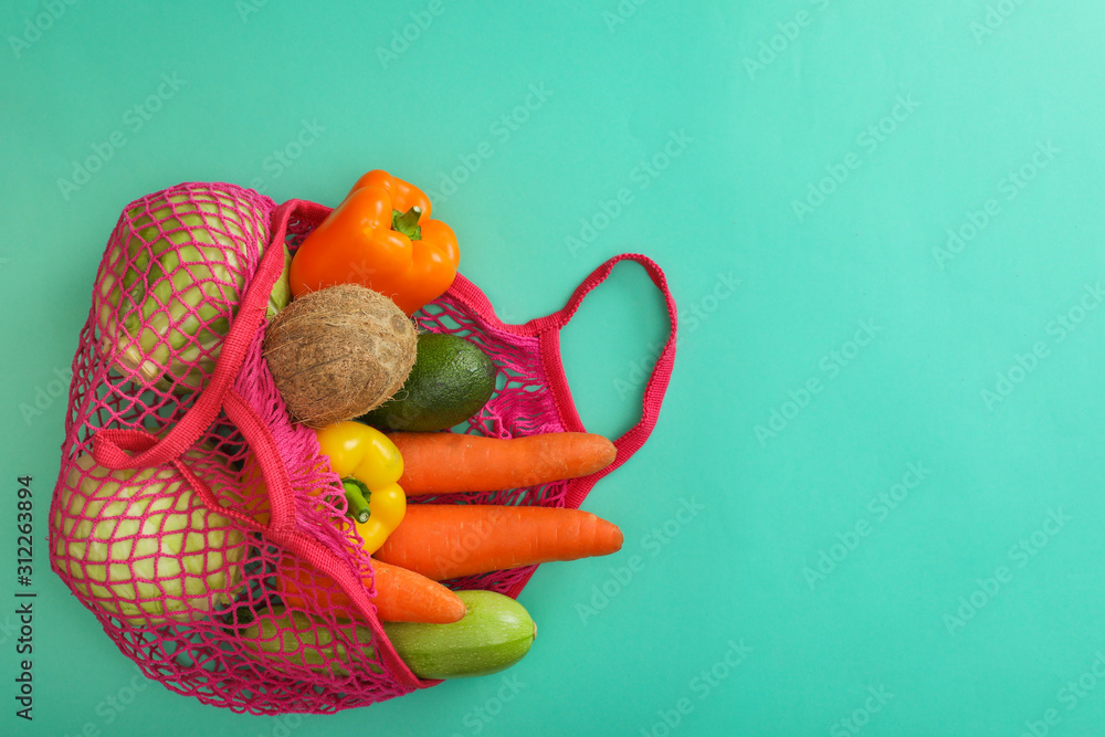 Net bag with fruits and vegetables on turquoise background, top view. Space for text
