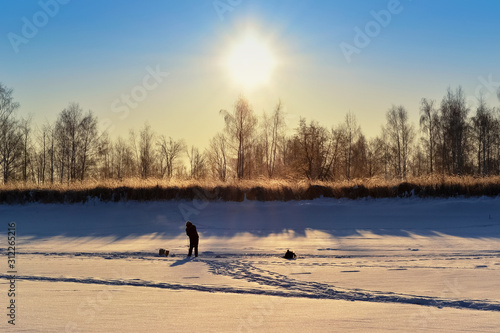 Silhouette of a lone fisherman on a snow-covered river  in the light of the rising sun
