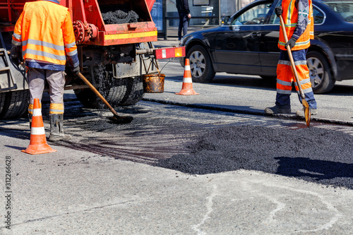 The group of road workers is repairing a section of the carriageway with fresh asphalt.