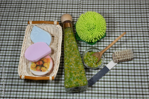 Items for cosmetic procedures - sea salt in a lying bottle and in a glass bowl with a wooden spoon, nail file, brush, washcloth in a green bowl, handmade soap in a wicker basket. photo