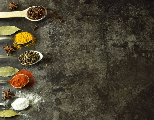 various spices and herbs on spoons on a dark background with free space for writing or recipes
