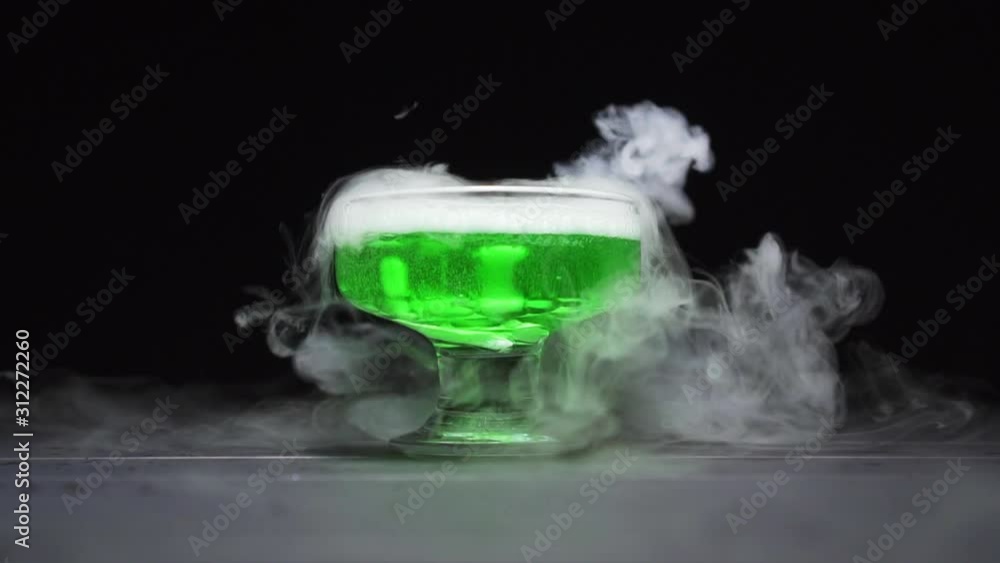 Green liquid boils emitting a lot of smoke in a glass bowl on a black background. Green liquid boils emitting a lot of smoke in a glass bowl on a black background.