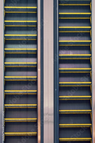 Parallel steel escalators at an airport, top-down elevated view.