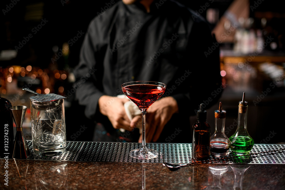 Professional male bartender serving the red alcoholic cocktail with ice cubes in the tall glass