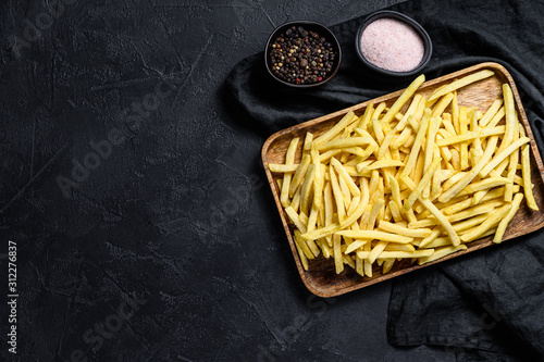 Frozen French fries in a wooden bowl. organic potatoes. Black background. Top view. Space for text photo