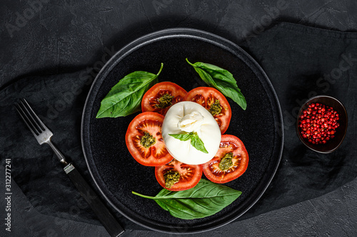 Burrata cheese and tomatoes salad served on black plate. Dark background. Top view