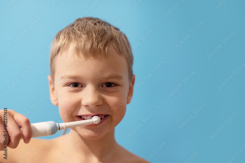 a boy brushes his teeth with an electric toothbrush on a blue background a boy brushes his teeth with an electric toothbrush on a blue background