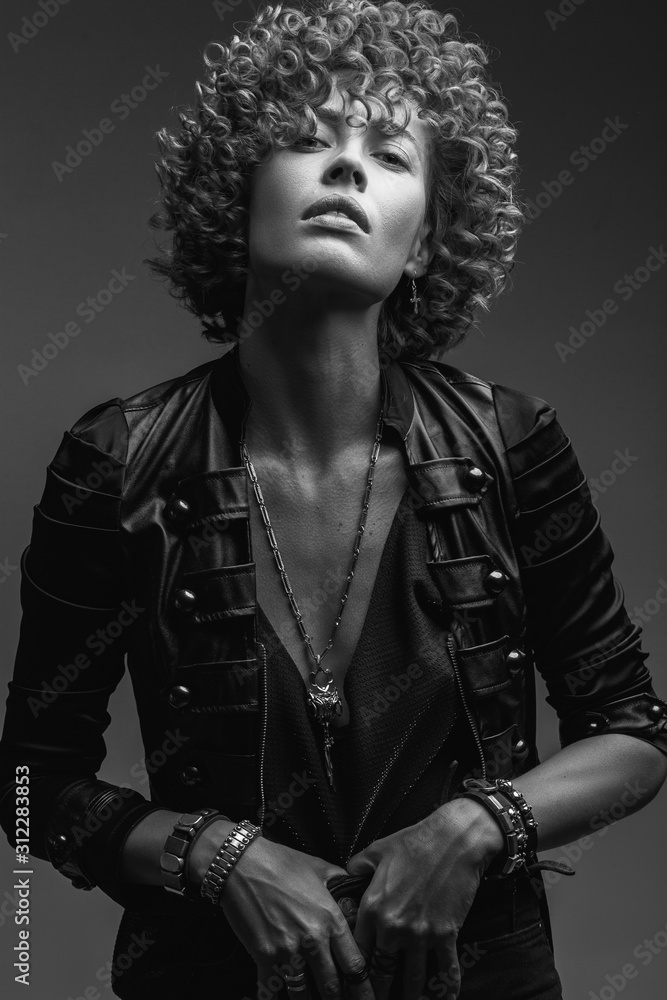 Young attractive sexy girl with curly hair in the form of a rock singer in a leather jacket. Black and white image Young attractive sexy girl with curly hair in the form of a rock singer in a leather jacket. Black and white image