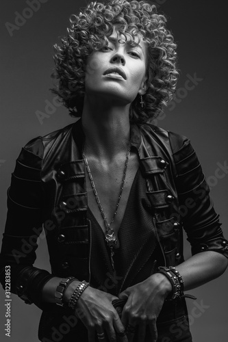 Young attractive sexy girl with curly hair in the form of a rock singer in a leather jacket. Black and white image