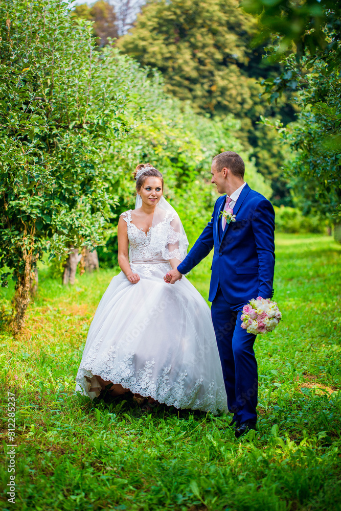 Happy smile bride and groom look at each other and running in the green garden. Wedding in the summer in the park. Happy wedding couple. Stylish and beautiful. Princess's dress