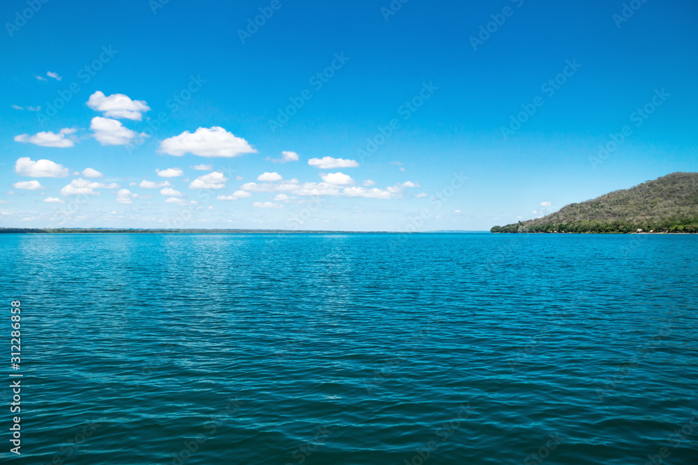 Lake Itza with cocodrile shaped mountain on sunny day, El Remate, Peten, Guatemala