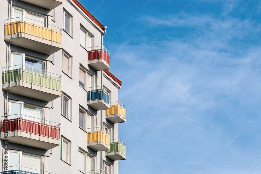 A light gray clean and tidy house building with colored balconies against a colorful blue sky.