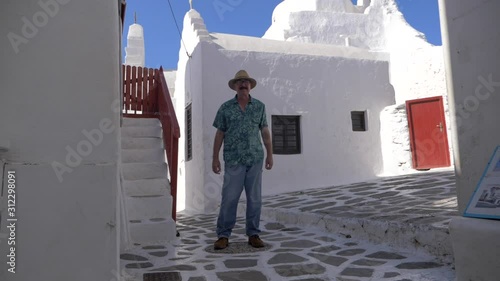 Mature man looking at camera, peacefully standing between antique Greek buildings, while feeling the wind around him in Mykonos, Greece. photo