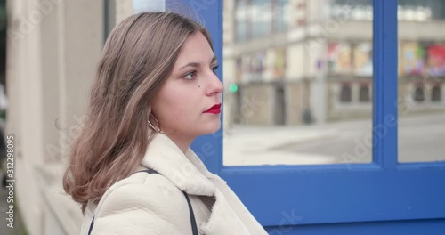 Beautiful young blond girl looking on the right, melancolic (close shot). She is wearing a white warm coat made of fake fur and has red lipstick on. Winter holidays, Flers, Normandy. photo