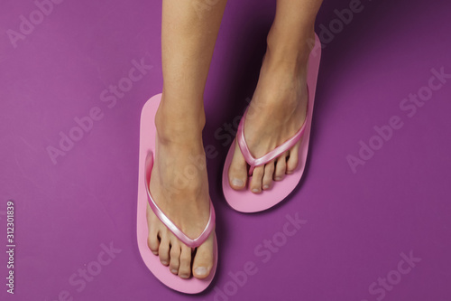 Minimalistic concept of beach holiday. Female legs with flip flops on purple background. Top view. Studio shot