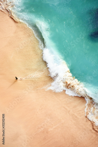 Fototapeta Naklejka Na Ścianę i Meble -  Stunning aerial view of a person running on a beautiful beach bathed by a turquoise sea during sunset. Kelingking beach, Nusa Penida, Indonesia. Nusa Penida is an island southeast of Bali, Indonesia.